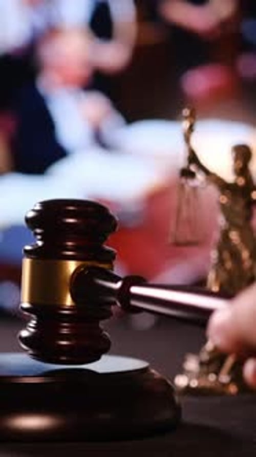 La main frappe avec force un marteau symbolisant la justice et les décisions juridiques dans une salle d'audience verticale