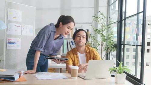 Two young Asian startup partners are working in a casual small business office.