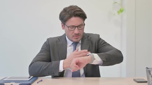 Empresario de mediana edad esperando comprobando el tiempo de guardia en la oficina
