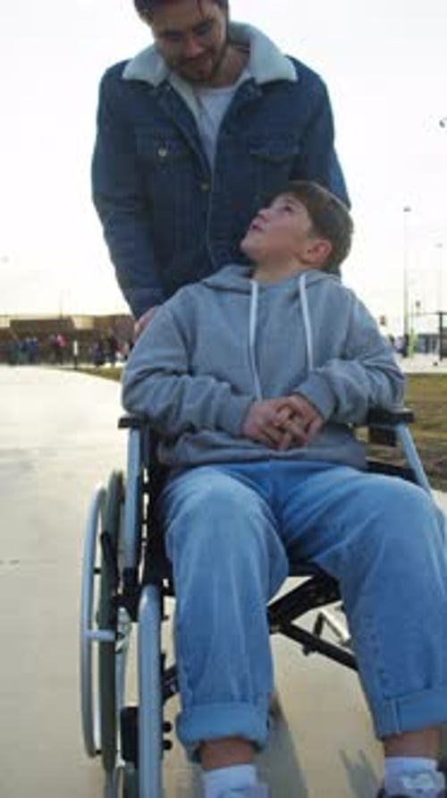 A Foster Care Worker Takes a Child with Special Needs Through a City Park in a Wheelchair