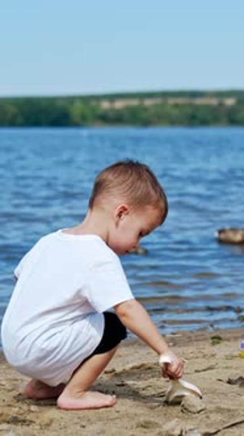 Small boy on river beach playing. Little child summer lifestyle. Vertical video