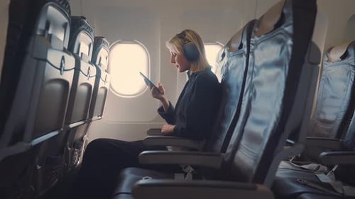 Young blonde woman with headphones using smartphone in airplane.