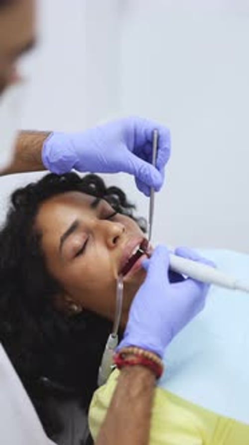 Vertical video of a male dentist removing dental tartar plaque from young patient using dental drill