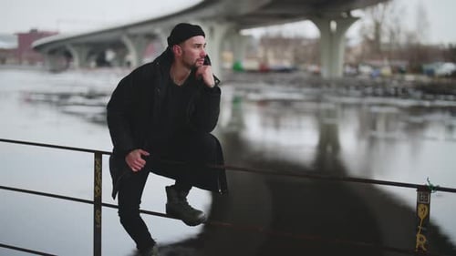 Winter in City Young Man Sitting Alone on River Embankment Zooming Shot Lonely and Selfconfident