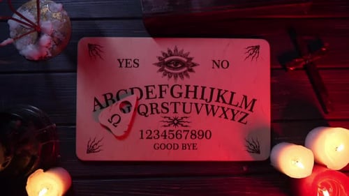 Close Up Video of a Wooden Ouija Board on a Table Surrounded By Candles Candlesticks and Other