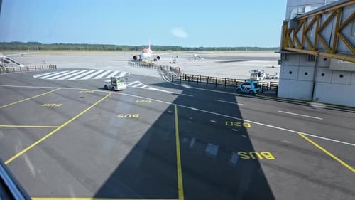 A parked airplane on a sunny day at the airport, with ground vehicles moving on the runway