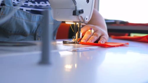 Adult Sewing Orange Fabric with a Machine