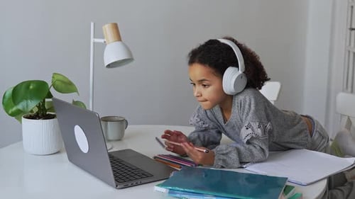 Primary School African American Student Child with Headphones Hand Writing in Book Using Laptop