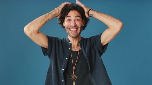 Wonder man put his hands on his head looking at camera isolated on blue background in studio