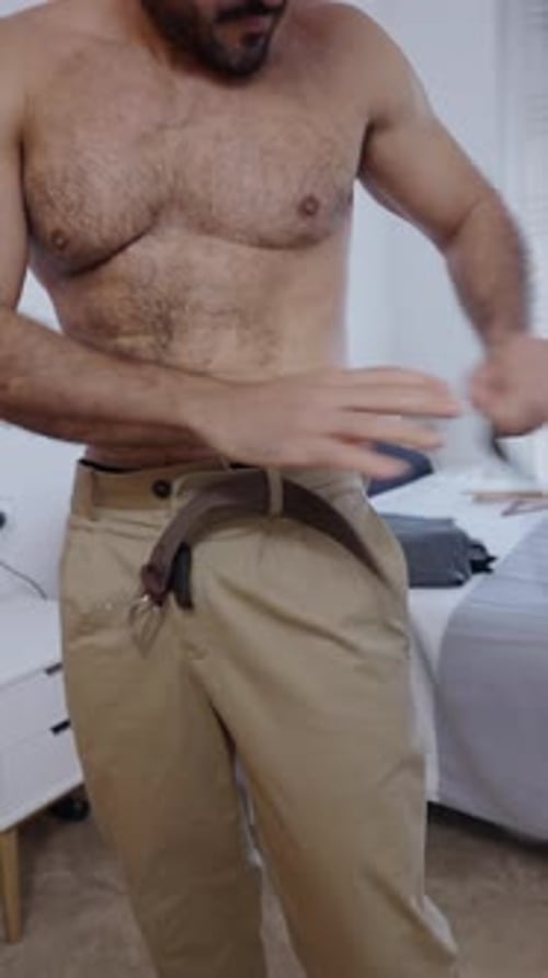 Hairy Man Adjusts His Belt in a Bedroom