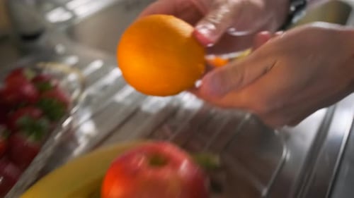 Men's hands washing different fruits in a stylish watch, close-up, preparing for a summer party.