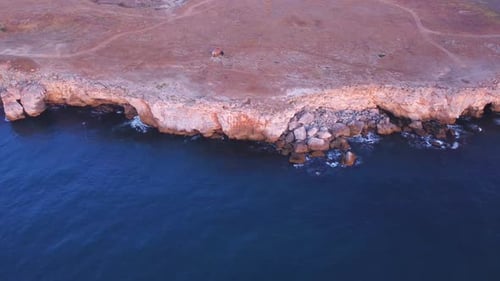 Top down aerial view of waves splash against rocky seashore, background. Flight over high cliffs of
