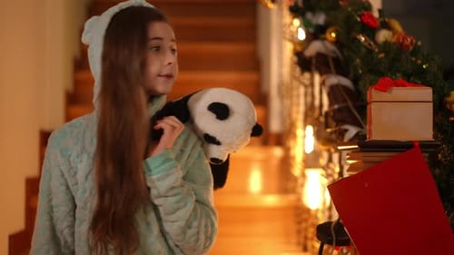 Girl in Pajamas Smiling with Panda Toy at Christmas