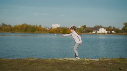 Preschooler Girl with Long Braids Throws Pebble Into River