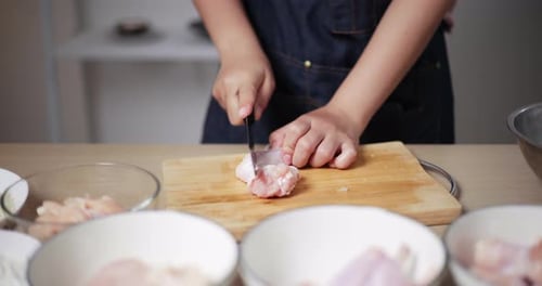Nahaufnahme der Hände einer jungen Asiatin, in Streifen geschnittene Hühnerflügel, die sich darauf vorbereiten, auf dem Tisch zu kochen.