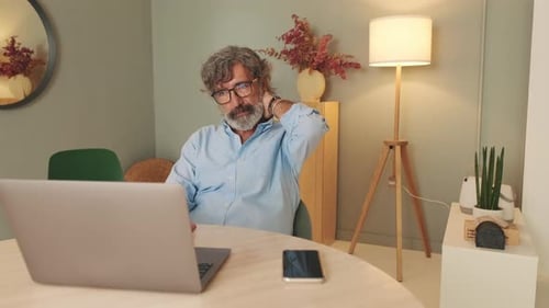 Man at Laptop Rubbing Neck Indoors