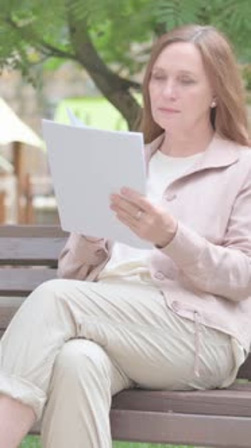 Woman Reads Document While Sitting on Park Bench