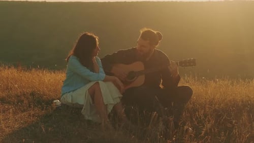 Man Playing Guitar for Woman in Grassy Field