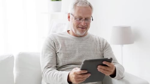 Senior Man Using Tablet Device on White Sofa