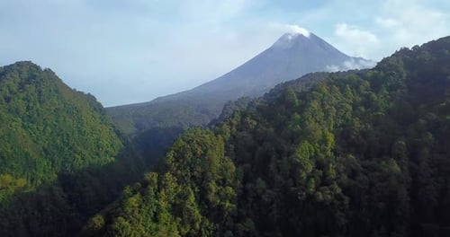 Slow aerial forward flight of wild forest and hill with mountain that emit smoke. Active volcano tha