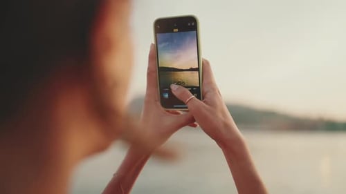 Close-up, girl stands on the embankment and takes pictures of sunrise on a mobile phone