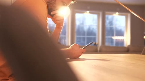 Man sits at table at home looking at mobile phone with anxious expression. Dolly right shot.