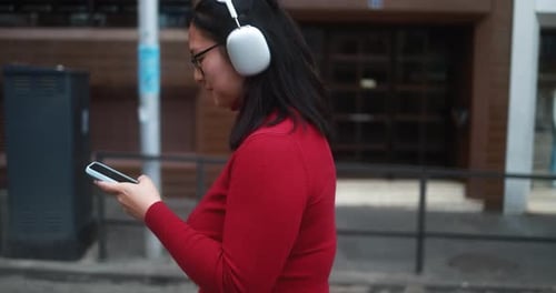 Woman using phone and wearing headphones on street