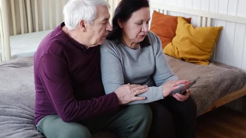 Senior Couple Looking at Phone on Bed