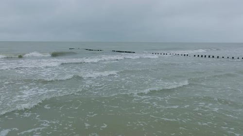 Aerial establishing view of an old wooden pier at the Baltic sea coastline, overcast winter day, whi