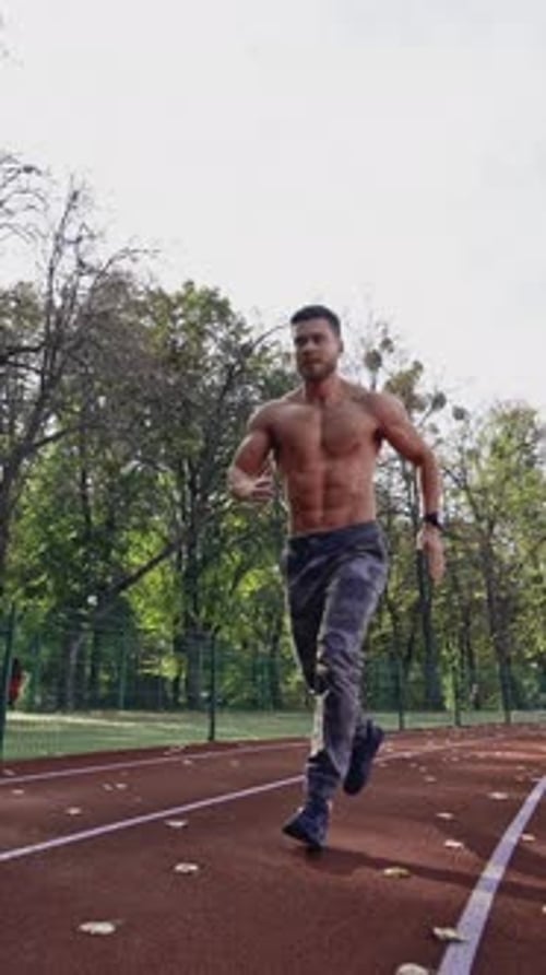 Handsome man training on the field stadium. Young muscular athlete runs on the sports track outdoors