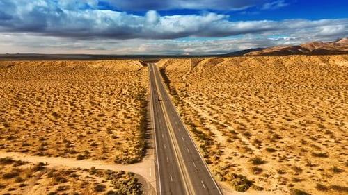 Drone moving above the four-lane highway in the dry desert. Arid landscape in California.