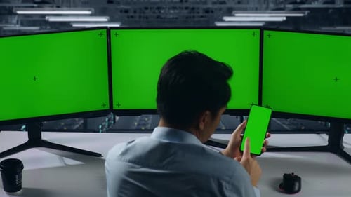 Asian Man Using Mobile Phone And Computer Monitor With Mock Up Green Screen In Data Center