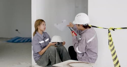 Asian woman engineer discusses site report with male supervisor using radio, reviewing blueprint,