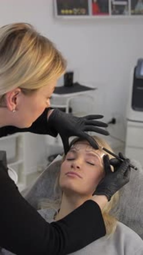 Woman Getting Eyebrows Shaped by Beautician in Studio