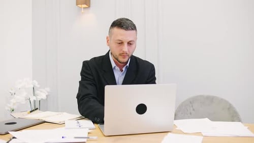 A Dedicated Professional Man is Diligently Working at a Modern Office Desk Equipped with a Laptop