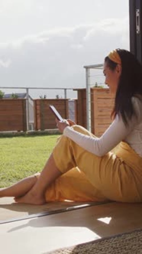 Vertical video: Using tablet woman scrolling, gazing to relax at patio with yellow band, copy space