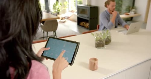 Woman Using Smart Home Application on Tablet While Man Works on Laptop