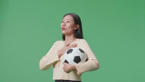 Side View Of Asian Woman With A Ball Singing National Anthem While Cheering Soccer On Green Screen