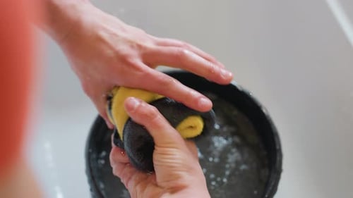 Hand Squeezing Yellow and Black Rag Above Water Bucket