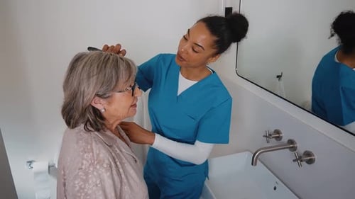 Caregiver helps senior woman in bathroom with grooming