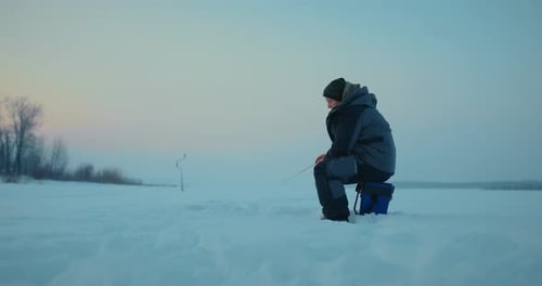 One Ice Fisherman Catching Fish By Rod in Ice Hole in Frozen River or Lake in Morning Prores
