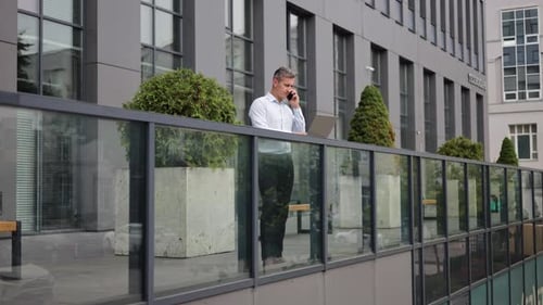 Man Talking on Phone Using Laptop Outside Office