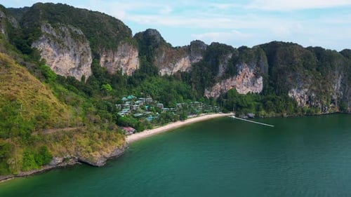 Beach by towering cliffs covered in green vegetation. Stunning aerial view flight drone