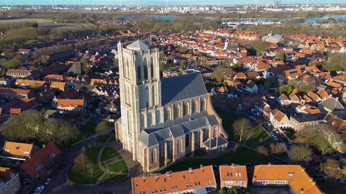 Aerial view of a historic town with a tall Gothic church in the center. Red-roofed houses