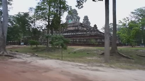 Panning shot of trees against ancient historic Hindu temple on sunny day - Siem Reap, Cambodia