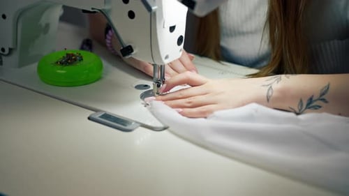 Close Up in the Sewing Workshop Young Girl Works with a Sewing Machine and White Fabric