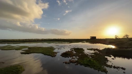 Golden sunset view of bog shallow marshlands lands with a small brick built building, Coastal scene