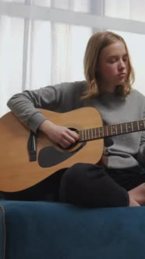 Teen Girl Practicing Acoustic Guitar at Home While Sitting on Couch and Playing Chords During Quiet
