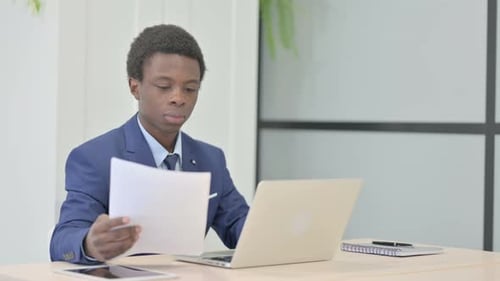 African Businessman Celebrating Success while Reading Documents in Office