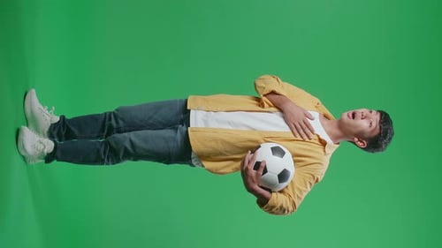 Side View Of Asian Boy With A Ball Singing National Anthem While Cheering Soccer On Green Screen